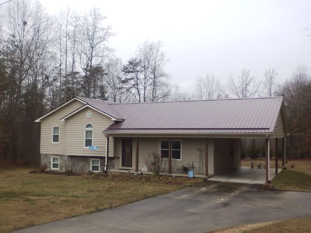 Burgundy metal roof on a tan split level home with an attached carport in Springdale